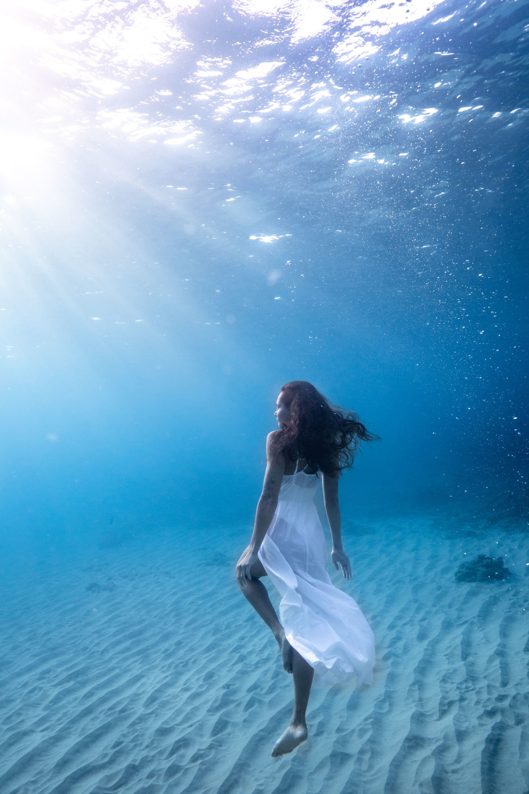 Underwater photography of a model in a white dress swimming in Hawaii