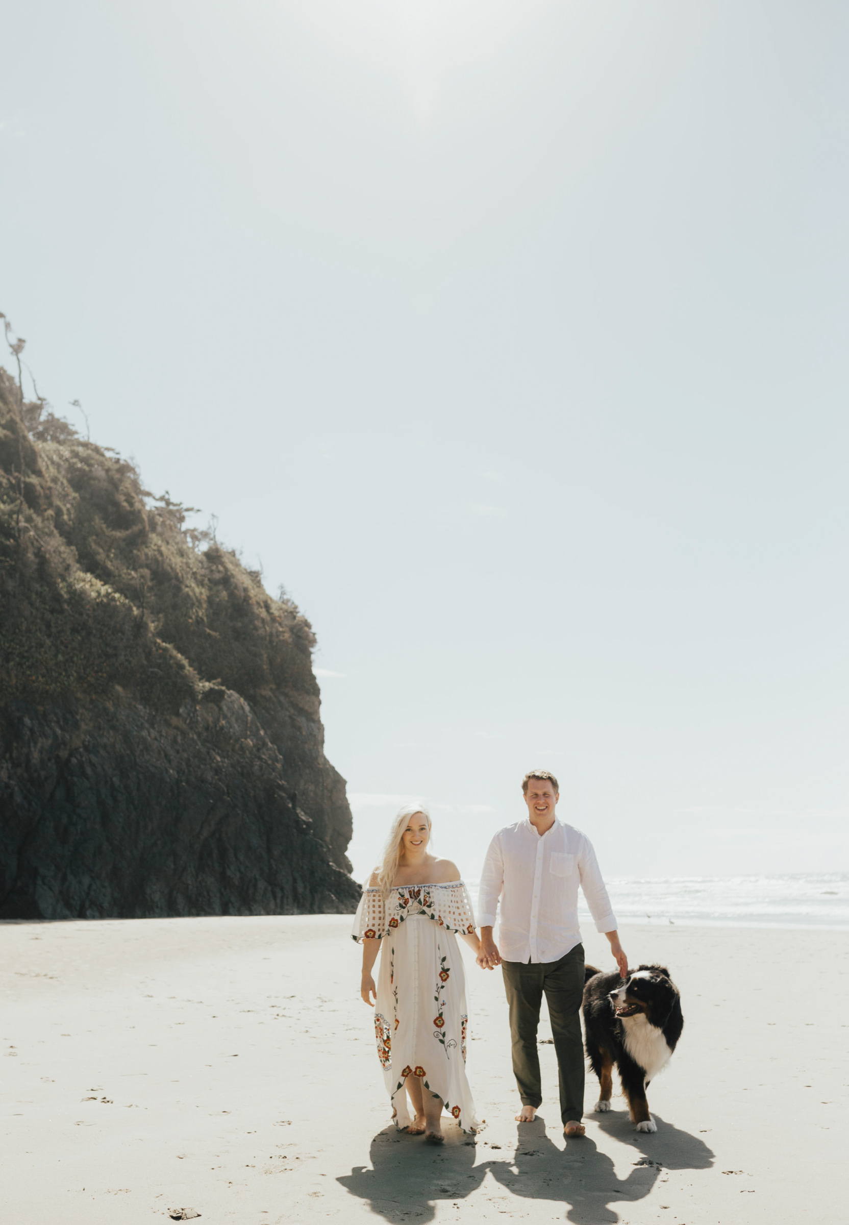 Maternity photography of a girl and her husband with their dog walking on a beach at the Oregon Coast