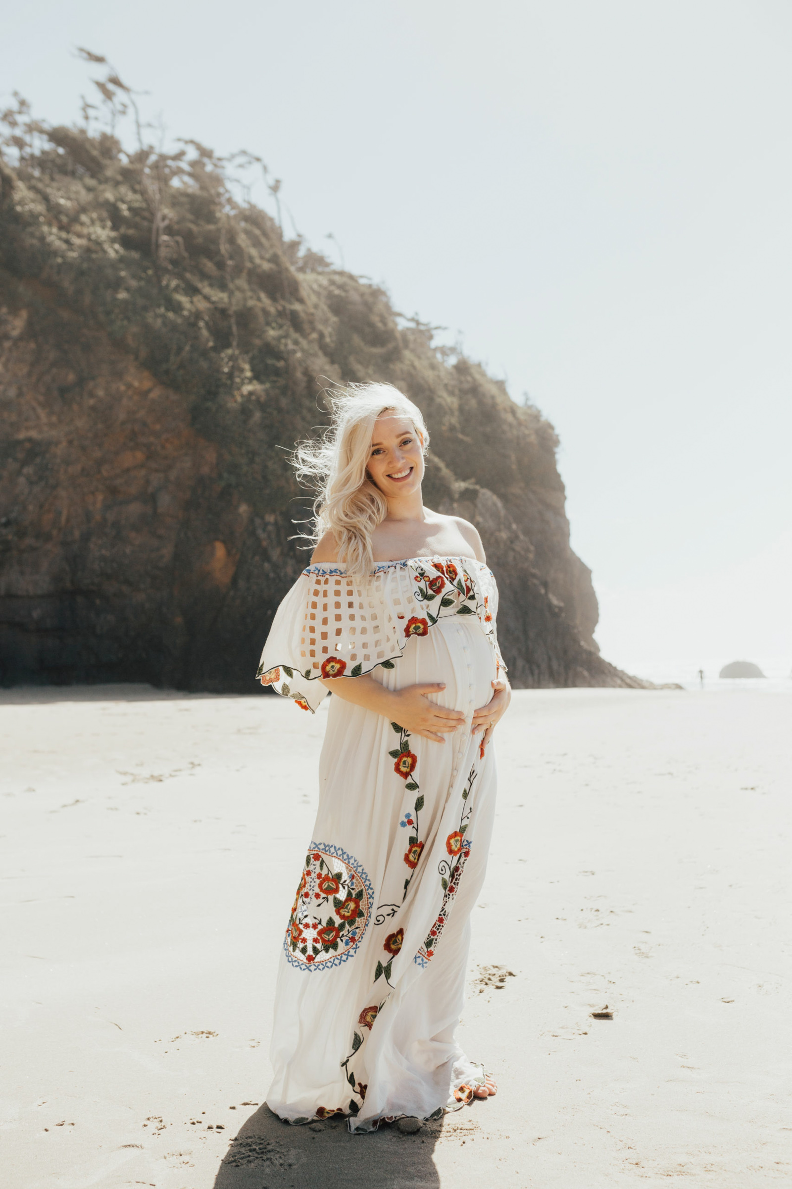 Maternity photography of a girl in wearing a dress standing on a beach at the Oregon Coast